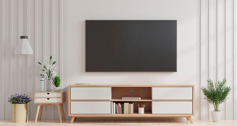 Living room containing light wood and white TV stand and pedestal styled with white decor items and a TV that is mounted to a white wall